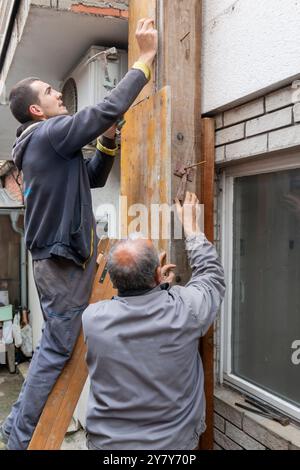 Der Arbeiter installiert und montiert Säulenschalungen für die Betonfüllung auf der Baustelle. Holzsäulenschalung mit Bolzen am Mauerwerk befestigt. Konz Stockfoto