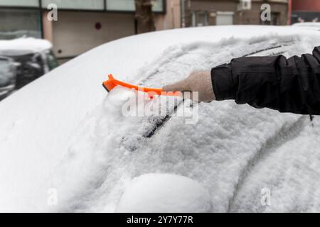 Fahrt im Winter. Nahaufnahme einer Hand, die die Windschutzscheibe eines Fahrzeugs von Eis und Schnee reinigt. Transport, Winter, Wetter, Menschen und Fahrzeug Stockfoto