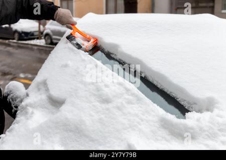 Fahrt im Winter. Nahaufnahme einer Hand, die die Windschutzscheibe eines Fahrzeugs von Eis und Schnee reinigt. Transport, Winter, Wetter, Menschen und Fahrzeug Stockfoto