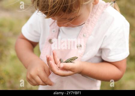 Kleines Mädchen, das eine Eidechse auf verschwommenem Hintergrund hält. Kind genießt wunderschöne Natur Stockfoto