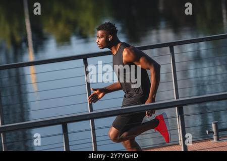 Konzentrierter junger afrikanischer Mann in Sportbekleidung, der am Ufer läuft Stockfoto