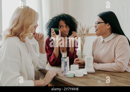 Drei reife Frauen diskutieren Schönheitsbehandlungen, während sie zusammen am Schreibtisch sitzen Stockfoto