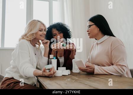 Drei reife Frauen diskutieren Schönheitsbehandlungen, während sie zusammen am Schreibtisch sitzen Stockfoto