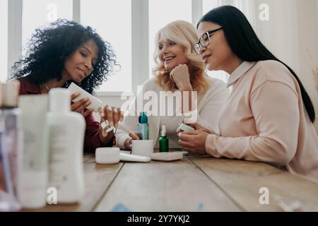 Drei glückliche reife Frauen testen Kosmetikprodukte, während sie zusammen am Schreibtisch sitzen Stockfoto