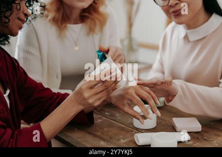Nahaufnahme von Reifen Frauen, die Kosmetikprodukte testen, während sie zusammen am Schreibtisch sitzen Stockfoto