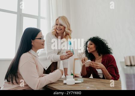 Glückliche reife Frau, die ihren Freunden Kosmetikprodukte rät, während sie Zeit miteinander verbringt Stockfoto