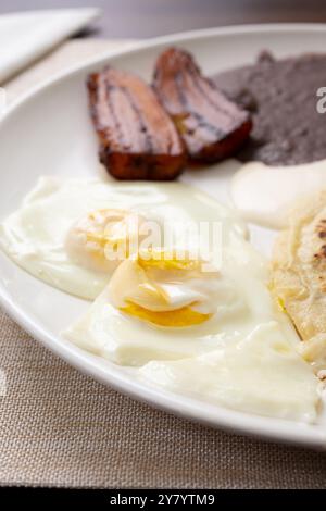 Blick aus der Nähe auf einen lateinamerikanischen Frühstücksteller mit sonnigen Eiern und gebratenen Kochbananen. Stockfoto