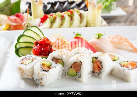 Blick auf einen Teller mit Lachsavocadorollen und einer Vielzahl von Nigiri, mit mehr Sushi-Brötchen im Hintergrund. Stockfoto