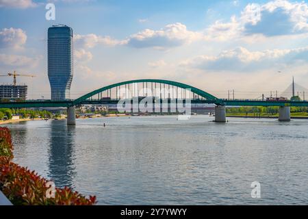 Die berühmte Alte Sava-Brücke überspannt den Fluss Save in Belgrad und bietet einen Blick auf die umliegende moderne Architektur und das üppige Grün unter hellem Himmel. Stockfoto