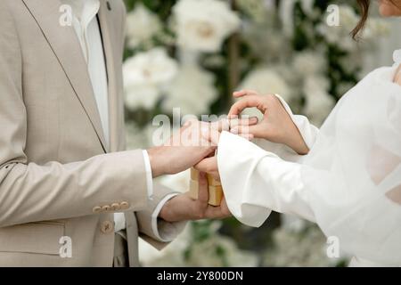 Ein Paar steht zusammen in einer atemberaubenden Blumenkulisse und tauscht Ringe aus, um ihr Gelübde der Liebe und Partnerschaft zu signalisieren Stockfoto