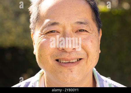 Lächelnder asiatischer Mann mittleren Alters genießt Sonnenschein im Freien, Nahaufnahme Porträt bei natürlichem Licht Stockfoto