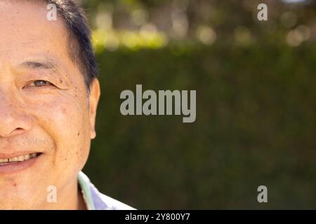 Lächelnder asiatischer Mann mittleren Alters im Freien mit Grün im Hintergrund, der sonnige Tag genießt Stockfoto