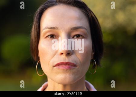 Nahporträt einer Frau mittleren Alters mit kurzen Haaren und Ohrringen, die im Freien ernst aussieht Stockfoto