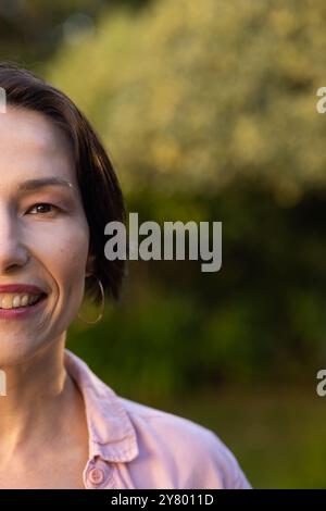Lächelnde Frau mittleren Alters mit kurzen Haaren, rosa Hemd und Creolen draußen, Kopierraum Stockfoto