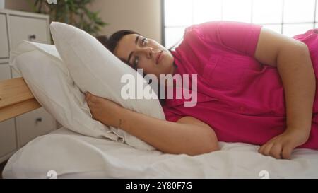 Frau, die drinnen ruht, rosa trägt, im Bett, im Schlafzimmer, zeigt Schönheit, Jugend und kurvige Gestalt, mit einem ruhigen, friedlichen Ausdruck, der einen rel widerspiegelt Stockfoto