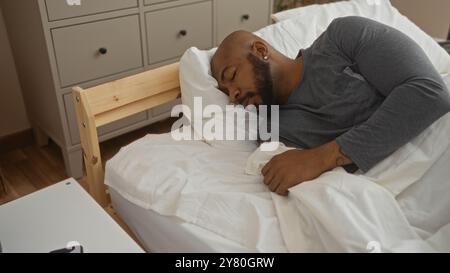 Hübscher junger afroamerikaner mit Bart, der friedlich im Bett in einem gemütlichen Schlafzimmer schläft Stockfoto