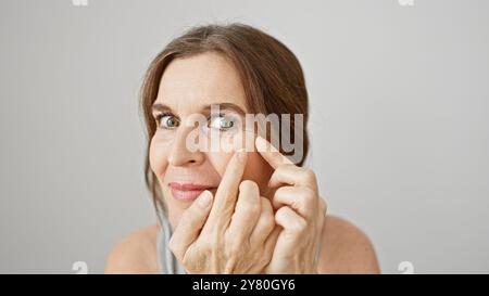 Frau mittleren Alters, die die Wange vor weißem Hintergrund drückt und Hautpflege oder Aknebehandlung darstellt. Stockfoto