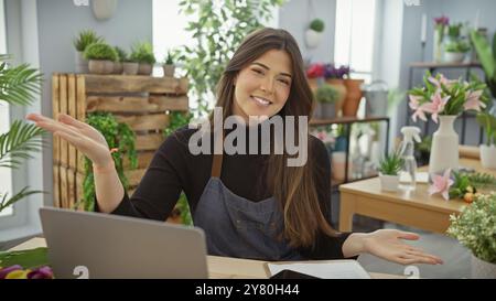 Lächelnde Blumenläuferin auf Schürze im Haus, umgeben von Pflanzen und Blumen in einem Blumenladen. Stockfoto