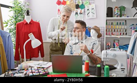 Zwei Schneider, ein Mann und eine Frau, arbeiten in einem geschäftigen Modedesignstudio zusammen, umgeben von Stoff und Nähwerkzeugen. Stockfoto