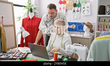 Zwei Schneider, ein Mann und eine Frau, arbeiten in einem bunten Atelier zusammen, umgeben von Mode-Design-Tools und Kleidungsstücken. Stockfoto
