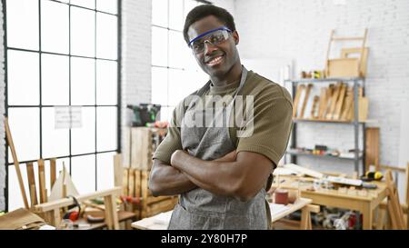 Selbstbewusster afroamerikanischer Zimmermann mit überkreuzten Armen in einer gut ausgestatteten Werkstatt Stockfoto