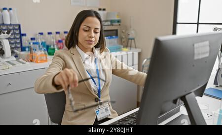 Eine professionelle hispanische Frau, die mit Mikroskop und Computer in einer modernen Laborumgebung arbeitet. Stockfoto