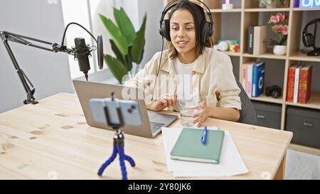 Hispanic Woman nimmt einen Podcast in einem Innenstudio mit Smartphone und Mikrofon auf. Stockfoto