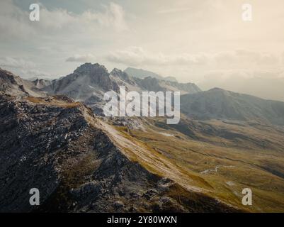 Drohnenblick auf die Savognin Berge in der Schweiz bei Sonnenuntergang mit Blick auf zerklüftete Gipfel und Täler, die in goldenes Licht getaucht sind Stockfoto