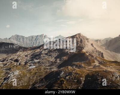 Drohnenblick auf die Savognin Berge in der Schweiz bei Sonnenuntergang mit Blick auf zerklüftete Gipfel und Täler, die in goldenes Licht getaucht sind Stockfoto