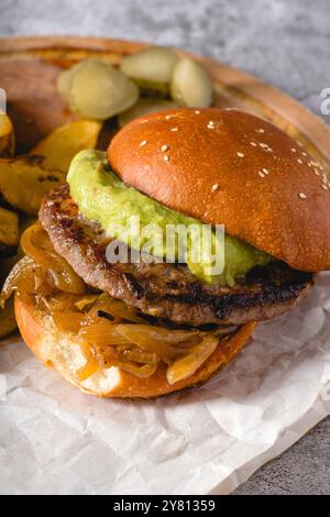 Burger mit karamelisierter Zwiebelsauce und Avocado auf einem Holzschneidebrett Stockfoto