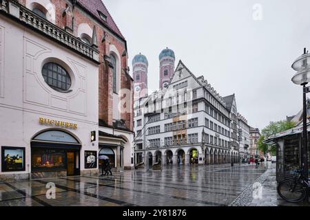 München - 18. April 2024: Außenansicht des größten Herrenmode-Hauses Hirmer. Die Türme der Frauenkirche Stockfoto