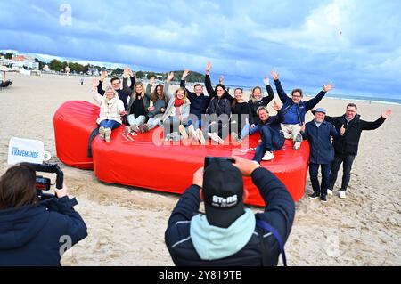 02. Oktober 2024, Schleswig-Holstein, Travemünde: Mitglieder des Tourismusverbandes Ostsee-Holstein-Tourismus sitzen bei der Präsentation der neuen Attraktion für die Nebensaison auf einer riesigen Warmwasserflasche am Strand von Travemünde. Foto: Jonas Walzberg/dpa Stockfoto