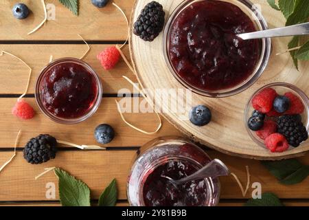 Natürliche Beerenmarmelade in Glasbehältern auf Holztellern und rustikaler Tisch mit Früchten und Blättern. Draufsicht. Stockfoto