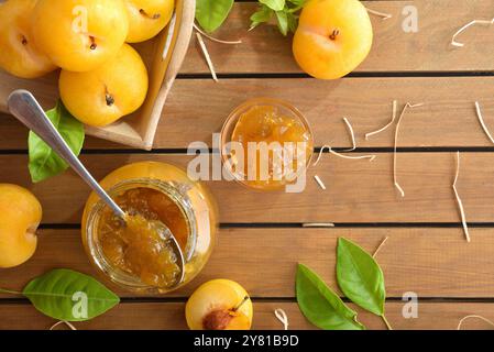 Hausgemachte natürliche Pflaumenmarmelade im Glasgefäß auf Holztisch mit Obststücken auf Tablett. Draufsicht. Stockfoto