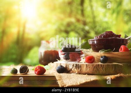 Natürliche Beerenmarmelade in Glasschale auf Holztellern auf rustikalem Tisch mit Früchten und Naturhintergrund. Vorderansicht. Stockfoto