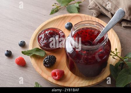 Konfitüren aus Waldfrüchten auf einem Holzteller auf einem Tisch mit Früchten und Blättern. Erhöhte Aussicht. Stockfoto