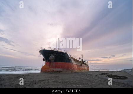 Ein verwittertes Schiff ist vor einem feurigen Sonnenuntergangshimmel auf dem goldenen Sand des Xigushui Beach geschildert. Der Kontrast zwischen dem lebendigen Himmel und dem dunklen Sch Stockfoto