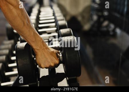 Muskulöser Athlet, der schwarze Hantel aus einem Rack im Fitnessstudio nimmt. Nahaufnahme. Stockfoto