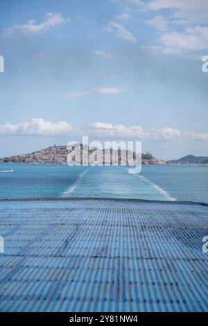 Idyllisches blaues Meer, blauer Himmel und der Hafen von Poros im Hintergrund, während die Fähre zum nächsten Ziel im griechischen Inselhopping fährt Stockfoto