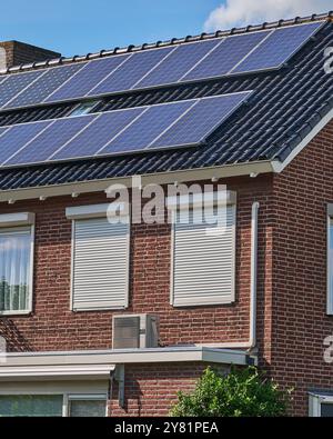 Moderne Luftwärmepumpe an der Außenwand eines Hauses mit Solarpaneelen auf dem Dach, die energieeffiziente Technologie für demonstrieren Stockfoto