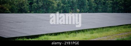 Ein großer Solarpark mit Reihen von Photovoltaik-Panels, neben einer Autobahn, in einer ländlichen Gegend mit Bäumen und blauem Himmel. Erzeugung erneuerbarer Energien Stockfoto