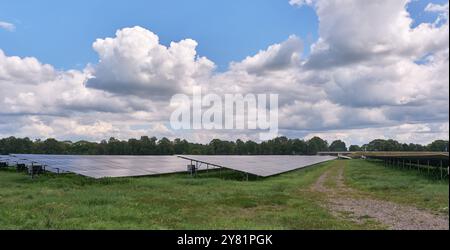 Ein großer Solarpark mit Reihen von Photovoltaik-Panels, neben einer Autobahn, in einer ländlichen Gegend mit Bäumen und blauem Himmel. Erzeugung erneuerbarer Energien Stockfoto