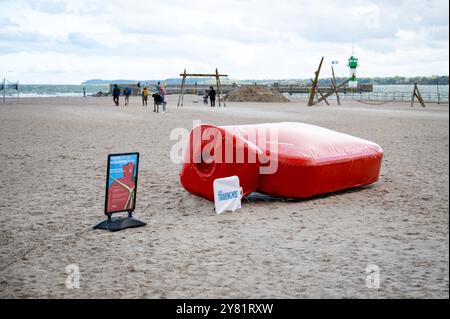 02. Oktober 2024, Schleswig-Holstein, Travemünde: Eine riesige Wärmflasche liegt am Strand als Attraktion des Tourismusverbandes Ostsee-Holstein-Tourismus für die Nebensaison. Foto: Jonas Walzberg/dpa Stockfoto