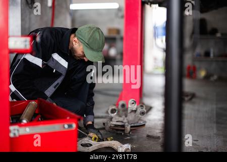 Ein Mechaniker mit grüner Kappe konzentriert sich auf die Reparatur eines Autoteils in einer professionellen Autowerkstatt und zeigt sein Engagement und sein technisches Können. Stockfoto