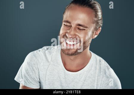 Ich habe etwas Lustiges mitgehört. Gut aussehender junger Mann, der vor grauem Hintergrund lächelt Stockfoto