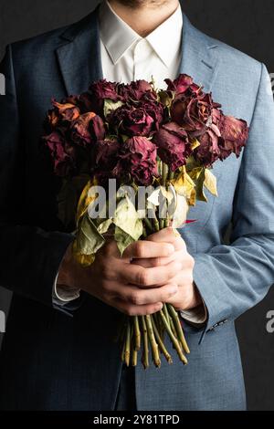 Mann im Anzug, der verblasste Rosen vor dem Konzept hält Stockfoto