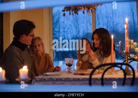 Die Familie genießt ein Abendessen bei Kerzenschein zu Hause während der Abenddämmerung vor der Kulisse des Schnees. Stockfoto