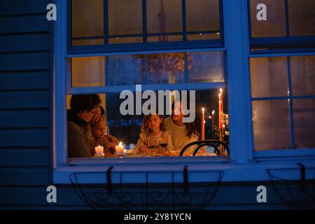 Eine vierköpfige Familie genießt ein Abendessen bei Kerzenschein am Fenster mit einem warmen Leuchten von innen Stockfoto