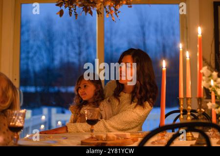 Eine Familie genießt ein gemütliches Abendessen bei Kerzenschein mit Blick auf den Dämmerungshimmel durch das Fenster. Stockfoto