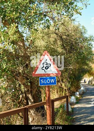 Ein rot-weißes dreieckiges langsames Schild mit einem Schneckensymbol an einer ländlichen Straße mit Laub im Hintergrund. Stockfoto